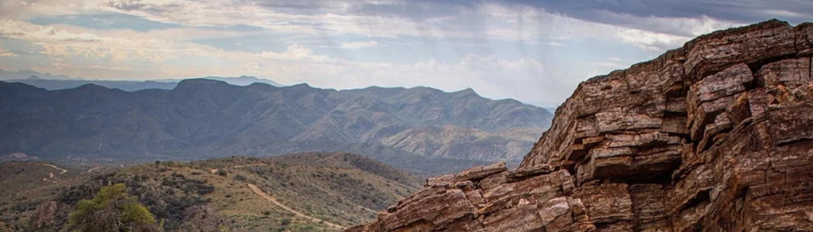 Rocky mountainside in the foreground with distant mountain peaks under a clear blue sky.