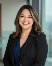 Professional headshot of a person in a suit with a dark, blurry background.