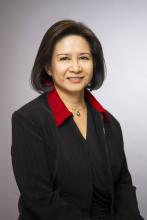 Professional headshot of a person in a suit with a dark, blurry background.