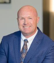 Professional headshot of a person in a blue suit with a patterned tie.