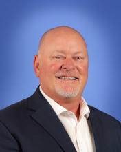 Professional headshot of a person in a suit against a blue background.