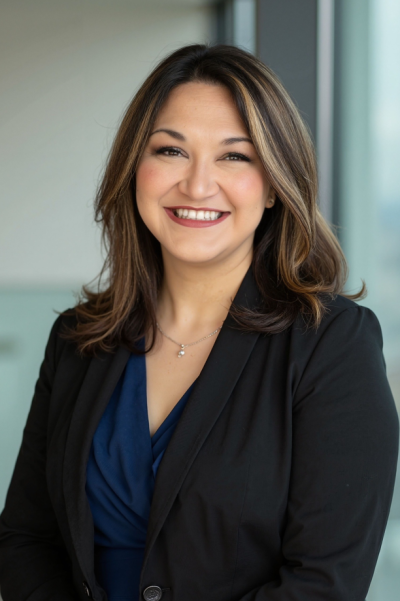Professional headshot of a person in a suit with a dark, blurry background.
