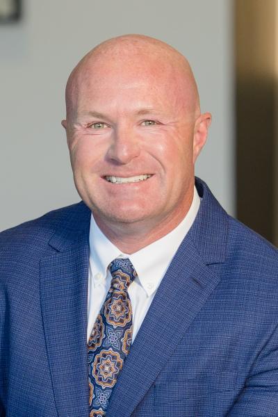 Professional headshot of a person in a blue suit with a patterned tie.