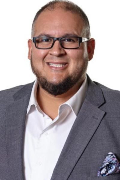 Professional headshot of a person wearing a gray suit and glasses, smiling.