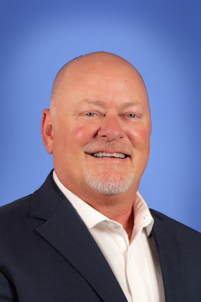 Professional headshot of a person in a suit against a blue background.